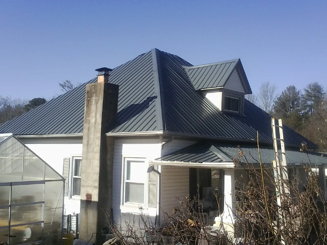 Dark blue standing seam metal roof on a white farmhouse with dormer — Slate & Tile Roof Repair by Roofing Brothers in Kirtland Afb