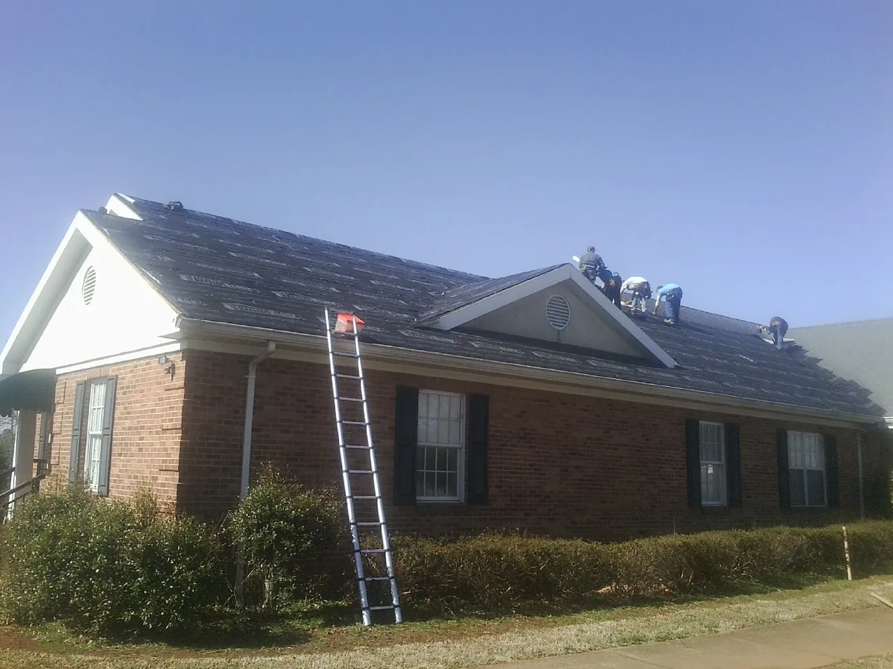 Crew tearing shingles off a brick ranch roof with a ladder set — Emergency Roof Repair work by our crew in Kirtland Afb