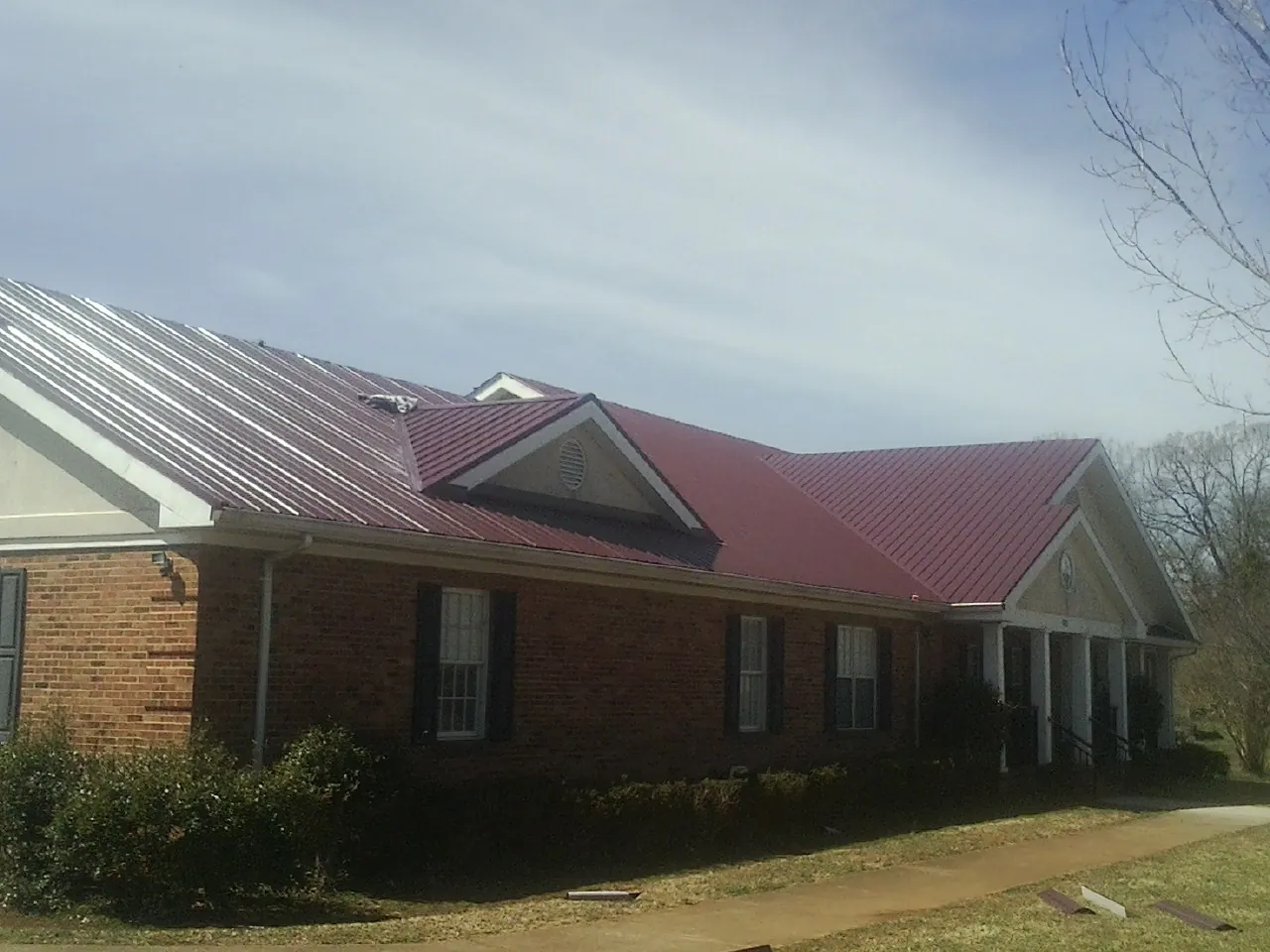Red metal roof with gabled entries on a long brick building, from a Hail Damage Roof Repair job in Kirtland Afb