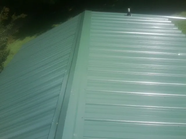 New green metal panels meeting at the ridge of a roof — Flat Roof Repair work by our crew in Kirtland Afb