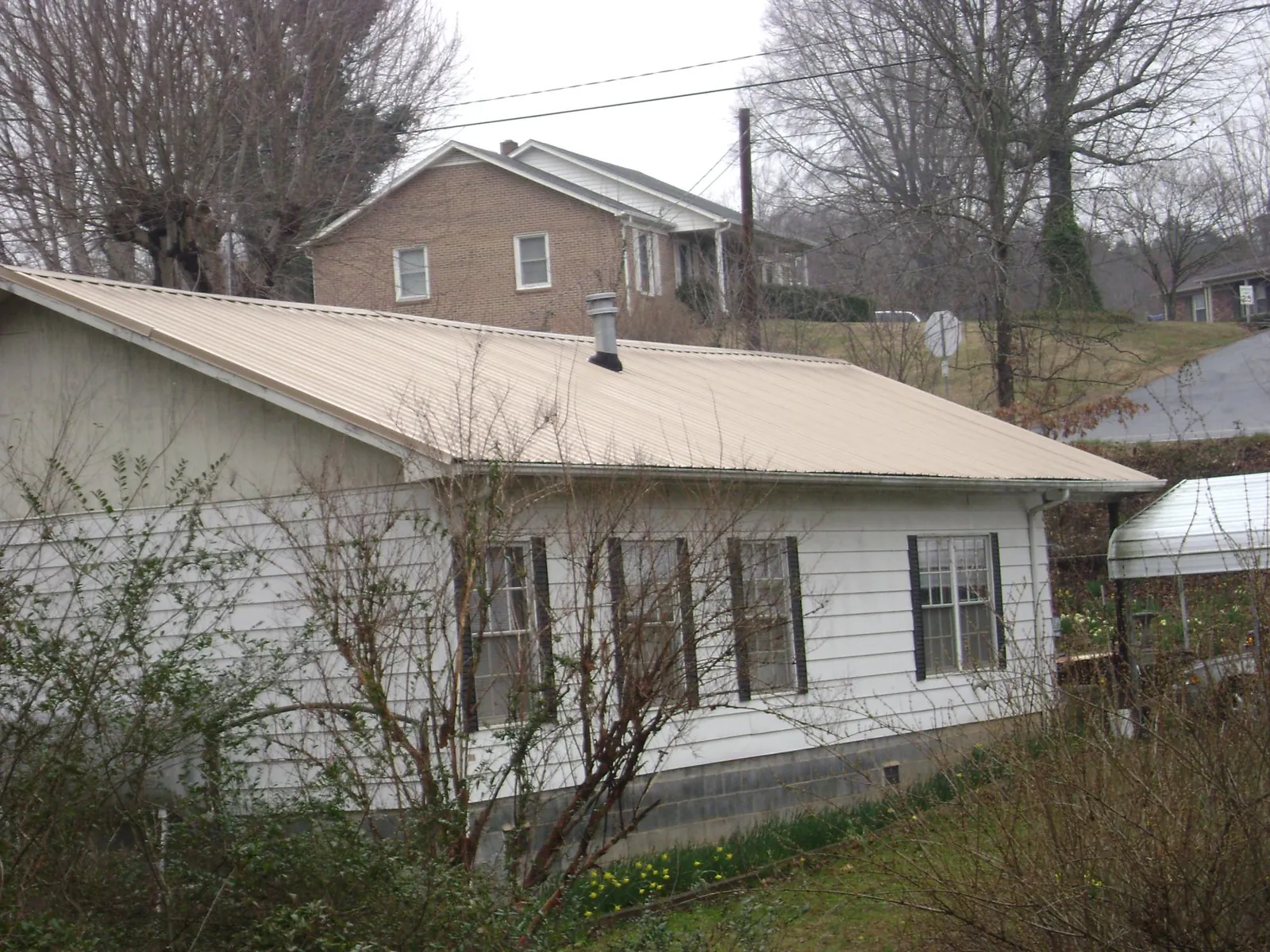 Tan metal roof on a white sided house set into a hillside — Commercial Roofing by Roofing Brothers in Kirtland Afb